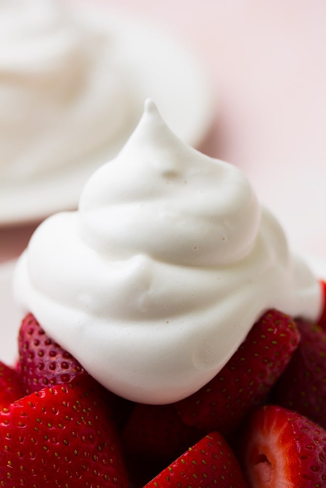 very close up shot of vegan whipped cream on a plate of strawberries with pink background