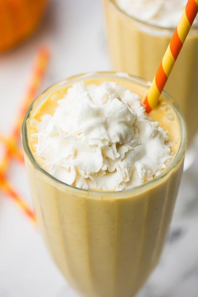 close up of top of pumpkin milkshake with whipped cream and colorful straw