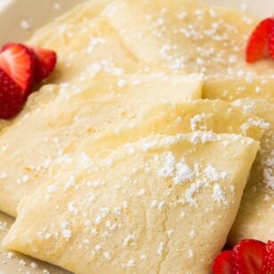 folded vegan crepes on a plate with powdered sugar and strawberries