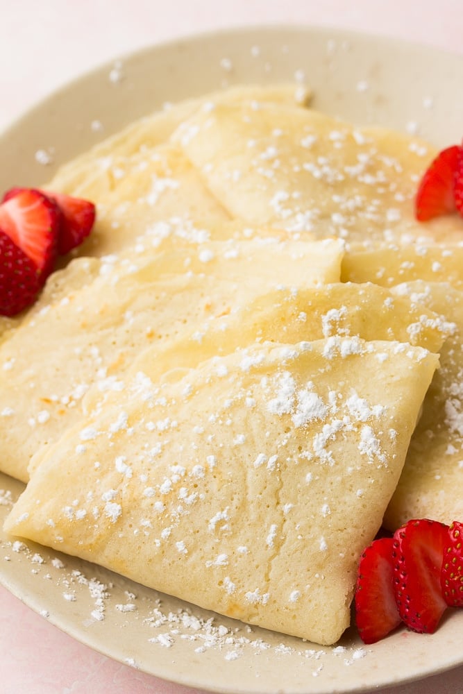 folded vegan crepes on a plate with powdered sugar and strawberries