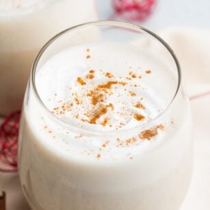 glass of vegan eggnog with spices sprinkled and red towel