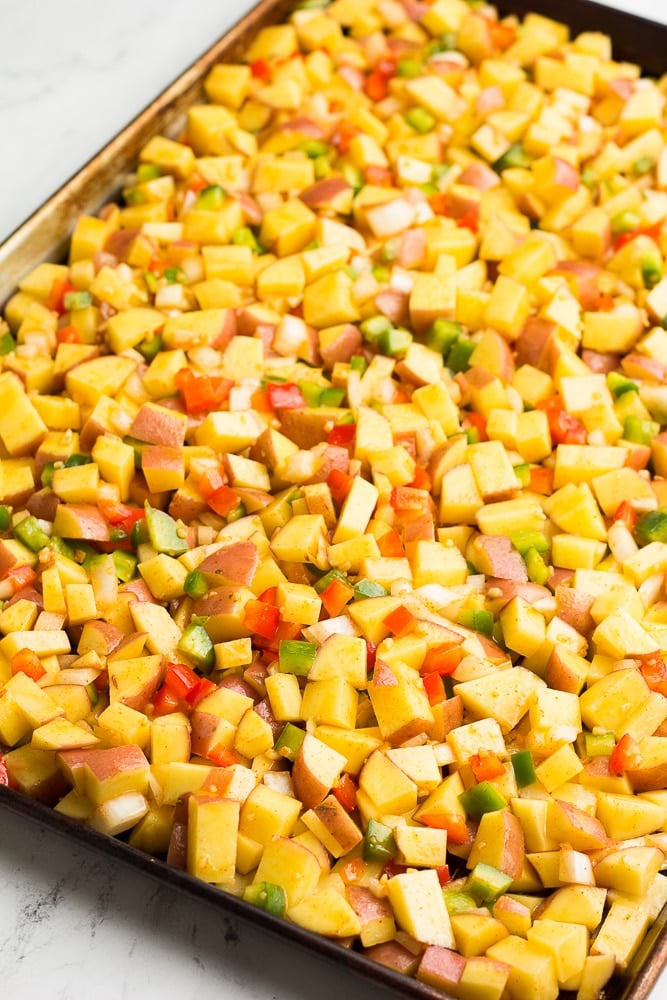 potatoes, peppers and onions on a baking sheet, uncooked.