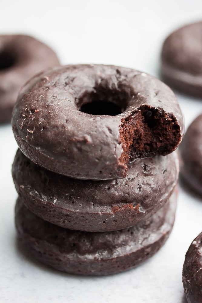 stack of 3 chocolate glazed donuts, bite taken out of top one, grey background