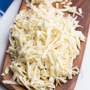 a cutting board with shredded mozzarella cheese and a blue towel