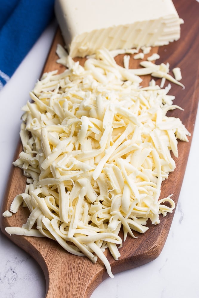 a cutting board with shredded mozzarella cheese and a blue towel