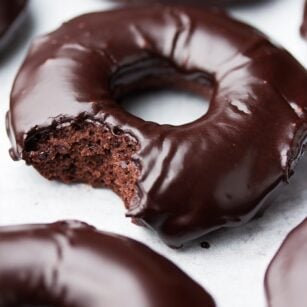 close up of a chocolate donut with glaze, a bite taken out of it