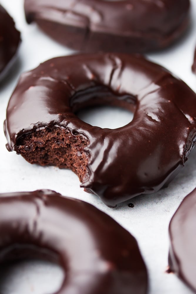 close up of a chocolate donut with glaze, a bite taken out of it