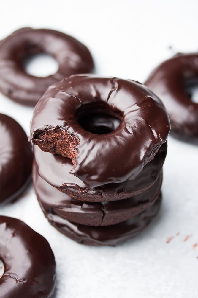 stack of 3 chocolate donuts with a bite taken out of the top one