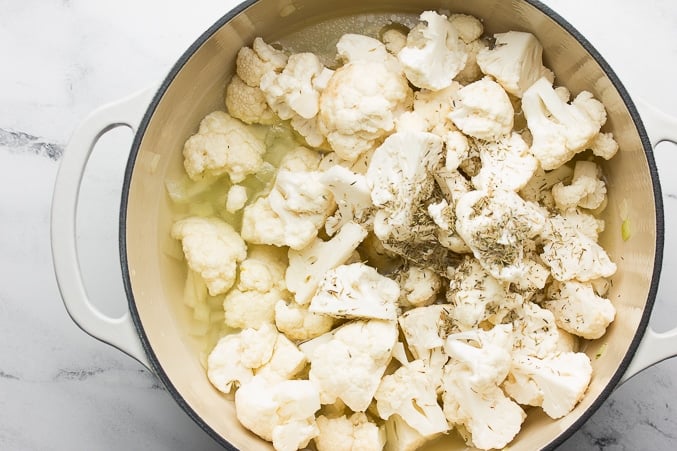 cauliflower and spices added to a white pot with onions and broth