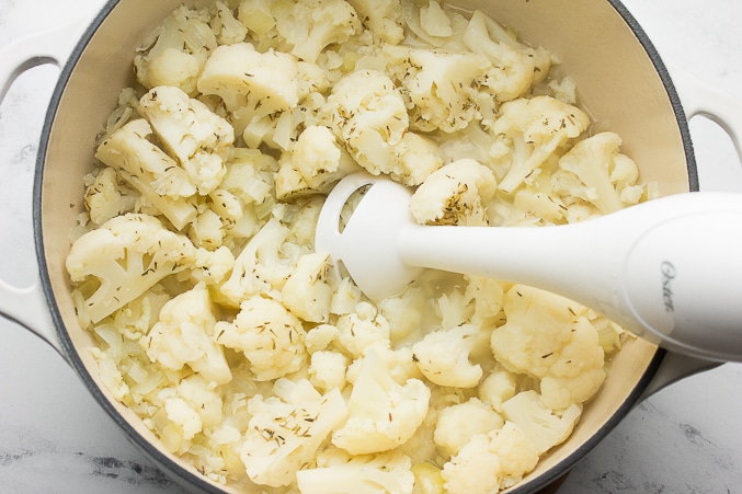 an immersion blender in pot of cauliflower soup, blending