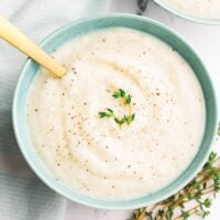 turquoise bowls with cauliflower soup with fresh thyme, white marble background