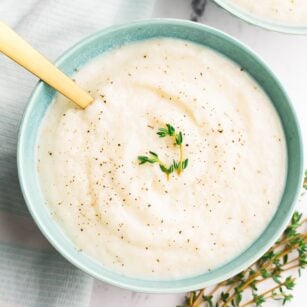turquoise bowls with cauliflower soup with fresh thyme, white marble background