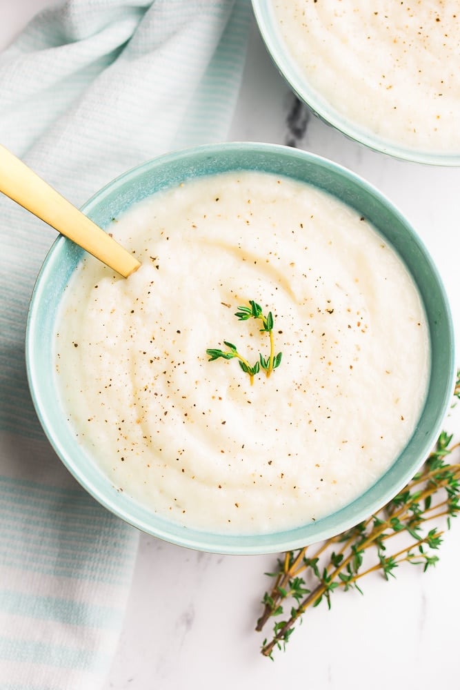 turquoise bowls with cauliflower soup with fresh thyme, white marble background