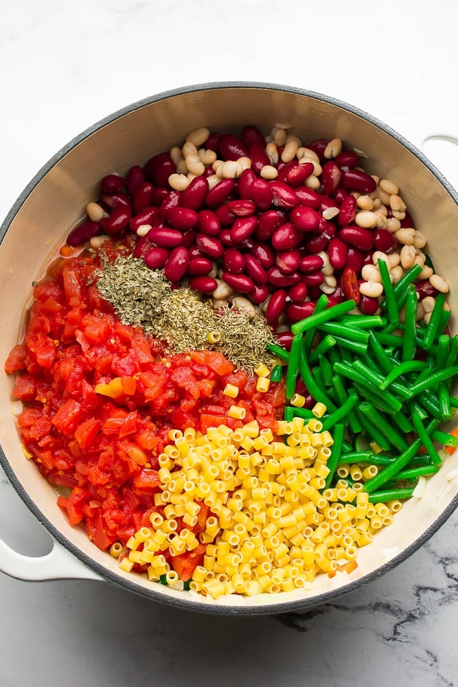 ingredients for vegan minestrone soup in a large white pot.