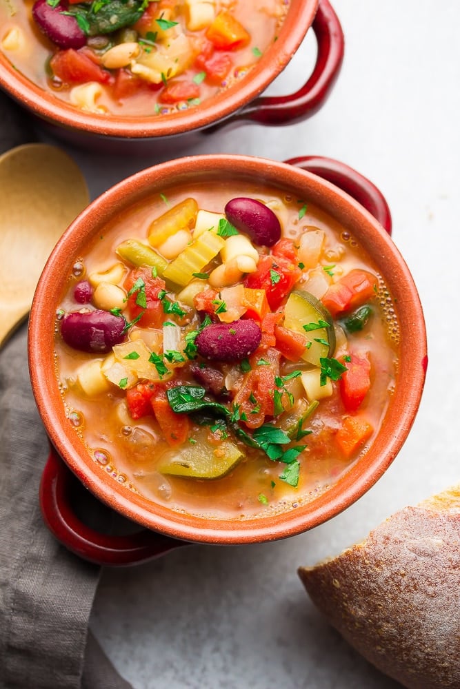 2 red bowls with filled with minestrone soup.