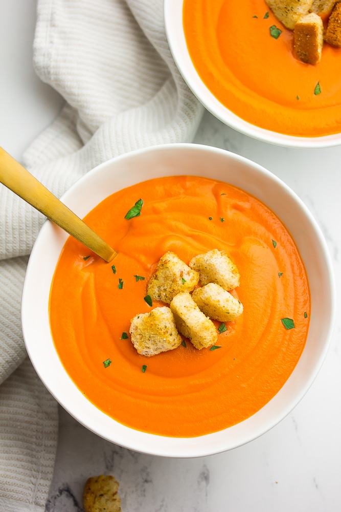 2 bowls of tomato soup with croutons and a gold spoon, white background