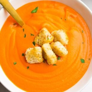 bowl of tomato soup with croutons and a gold spoon in it