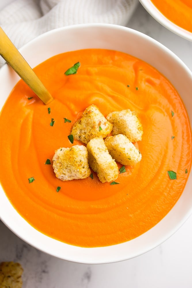 bowl of tomato soup with croutons and a gold spoon in it