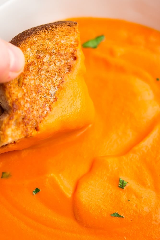 grilled cheese being dipped into bowl of soup