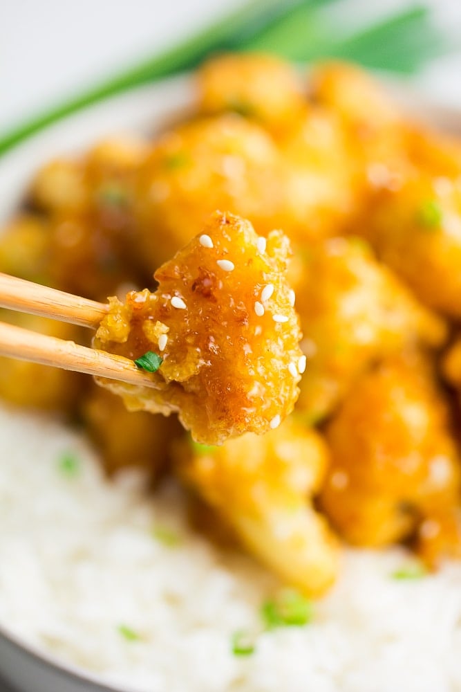 chopsticks holding a piece of cauliflower in sauce