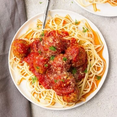 meatballs with red sauce on spaghetti on a plate with grey background
