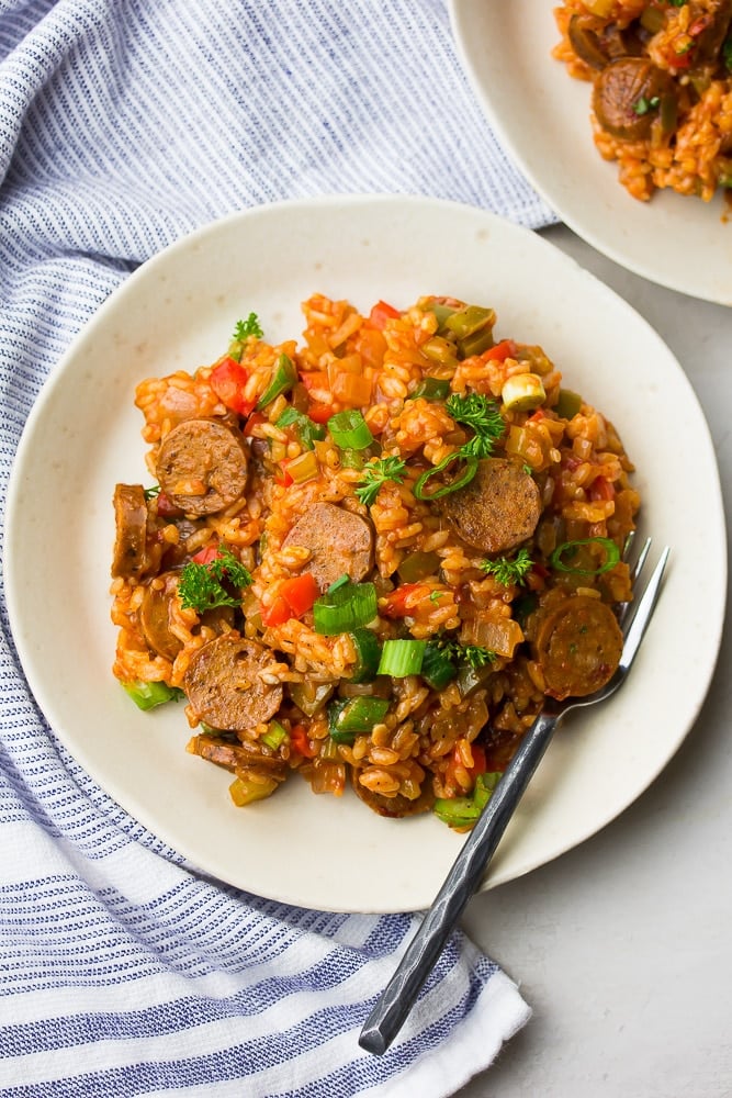 white plate with jambalaya on it, fork and blue striped towel