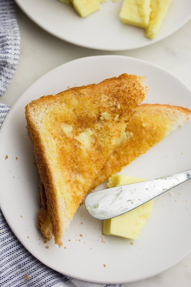 showing a piece of white bread toast with melted butter on it, knife nearby