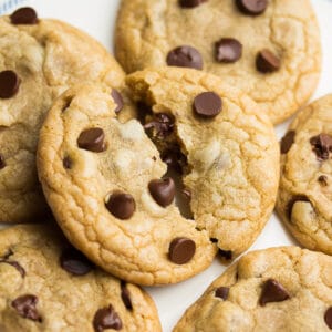 a square photo of a pile of chocolate chip cookies with the top one broken in half