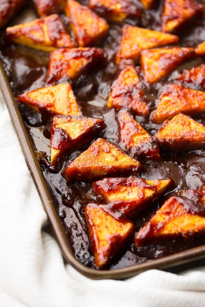 close up side shot of triangle tofu pieces with bbq sauce on them, cooked