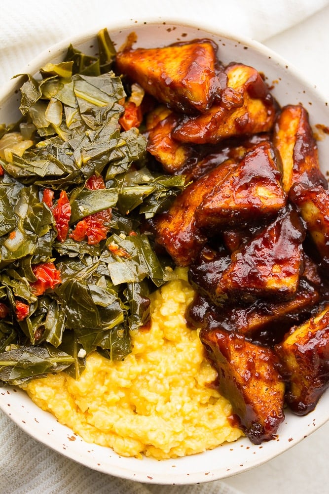 very close up of bbq tofu, collard greens and grits in a bowl