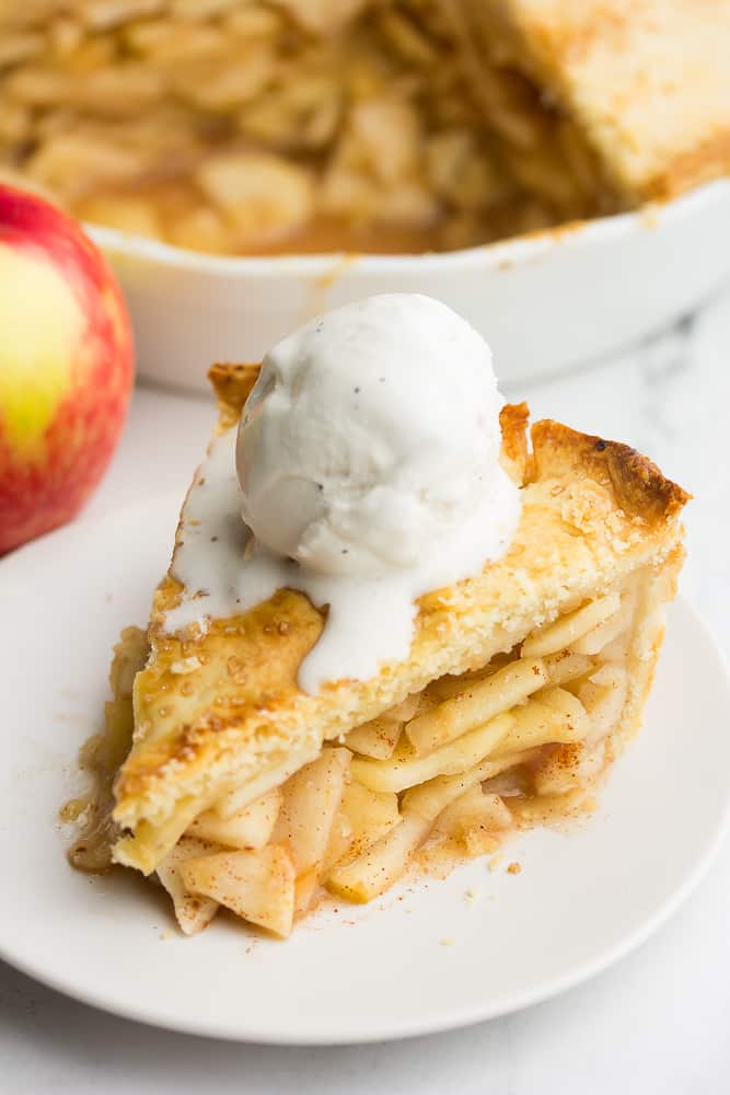 a piece of vegan apple pie on a plate with vanilla ice cream on top, melting