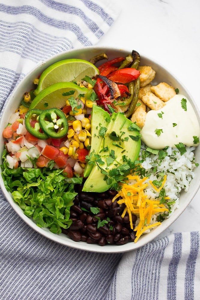 bowl with burrito bowl ingredients in it: rice, beans, queso, avocado, tofu.