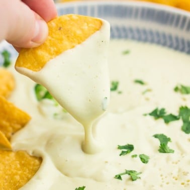 square photo of a chip dipping into bowl with white cheese sauce