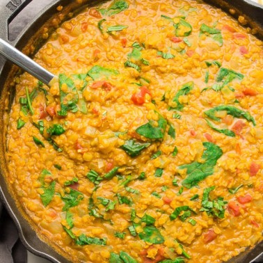 cast iron pan full of lentils and spinach, with a silver large spoon in it