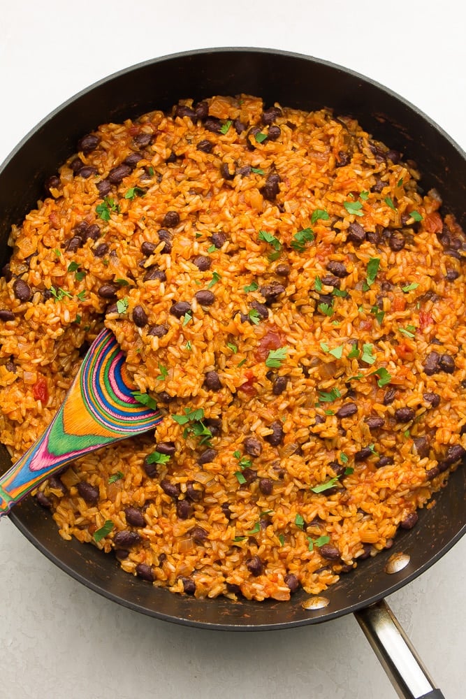 dark pan filled with rice and beans, cilantro on top, colorful spoon in it