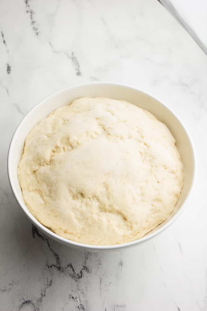 Risen pizza dough in a large white bowl