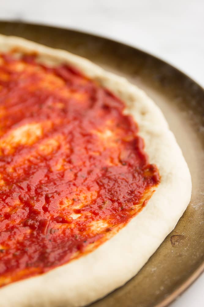 Close up of raw pizza dough covered in tomato sauce