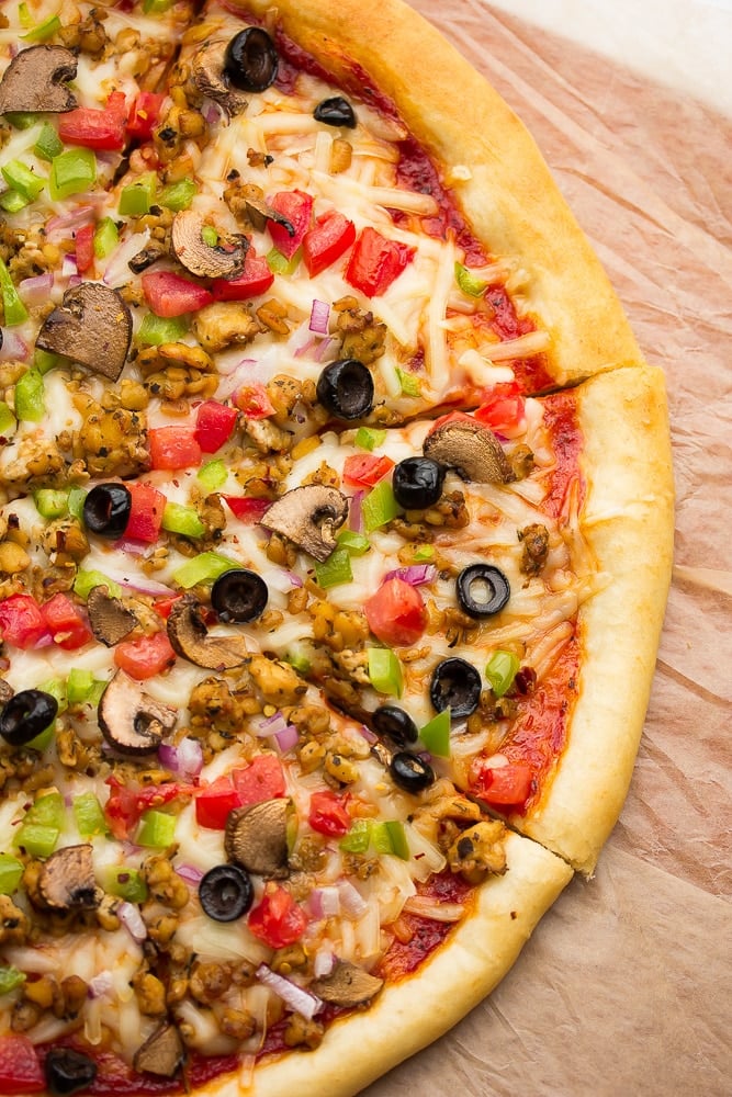 Close up of cooked vegan pizza with veggies, cheese, tempeh sausage, and tomato sauce