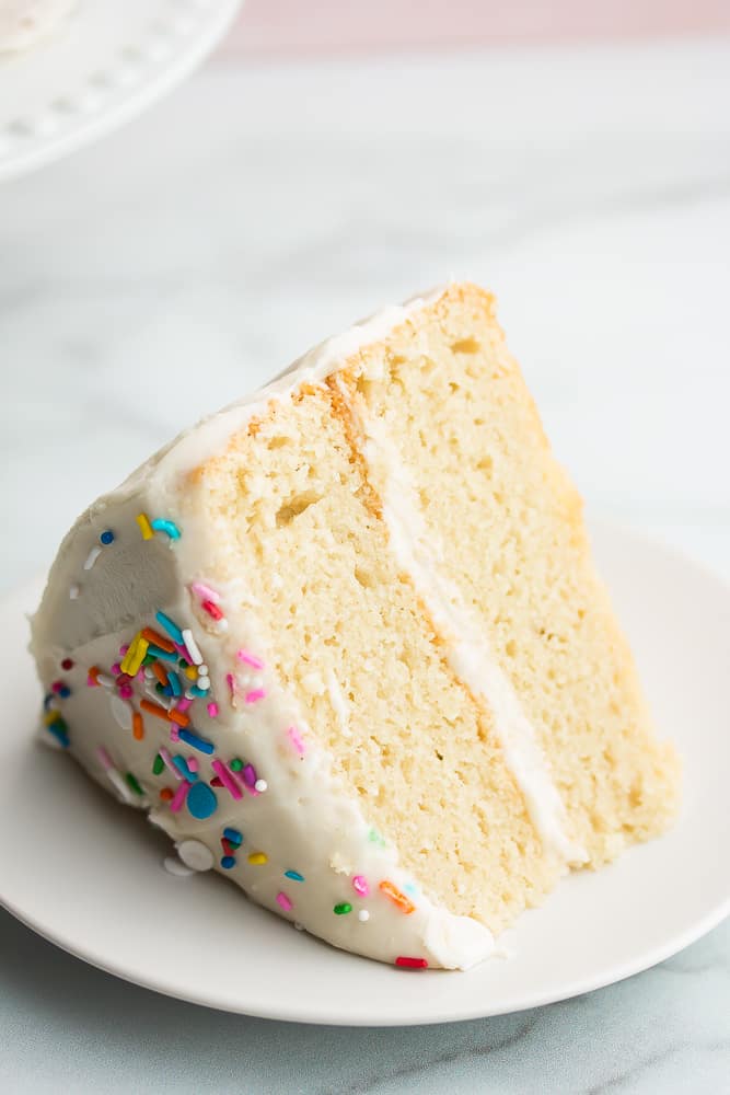 Close up of a slice of white cake with sprinkles on top on a white plate