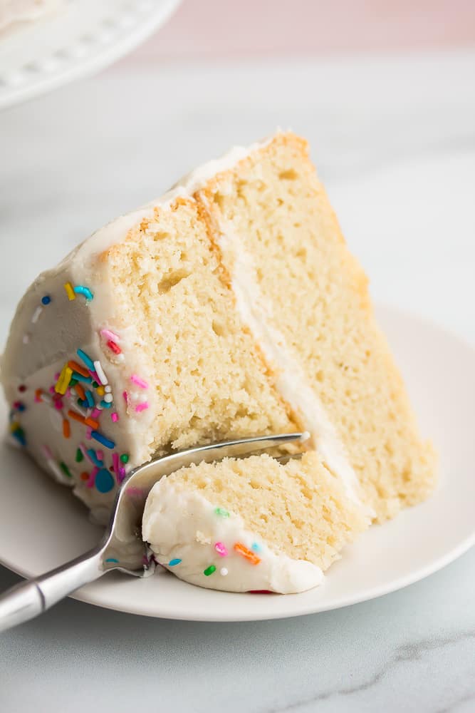 Close up of a slice of white cake with a fork taking a bite