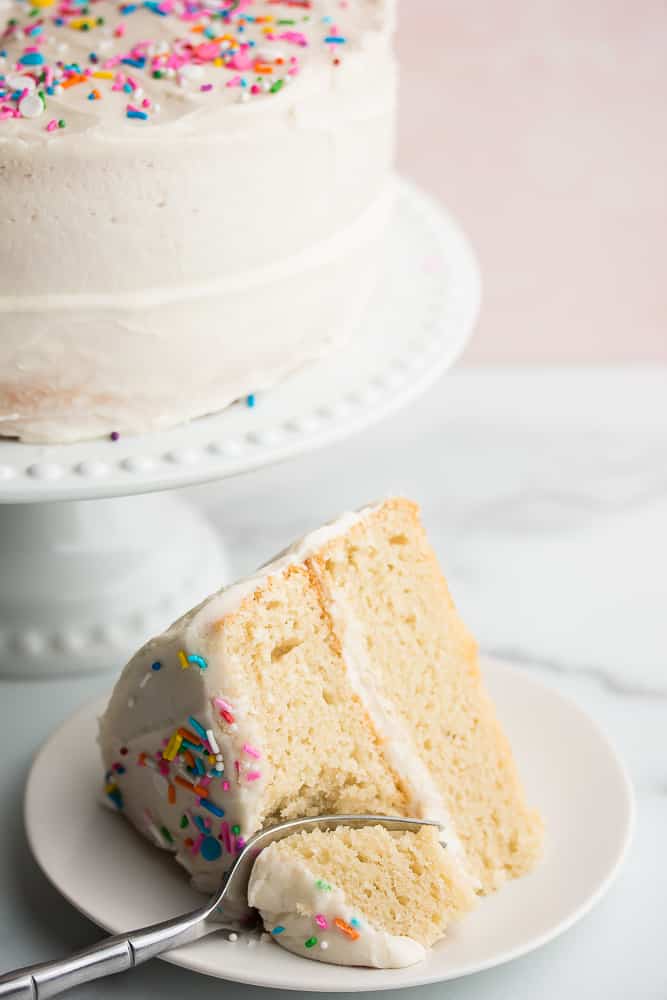 Fork taking a bite out of a big slice of white cake on a plate