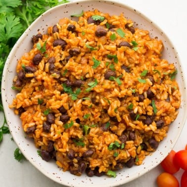 square image of a bowl of rice and beans, cilantro and tomatoes on the side
