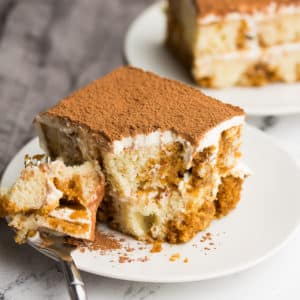 Fork taking a piece out of a slice of tiramisu cake on a white plate