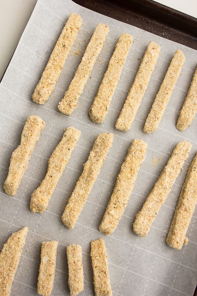 battered sticks of cheese on a baking sheet with parchment paper