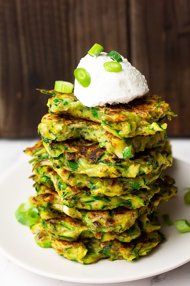 stack of fritters that are green with sour cream on top and chives