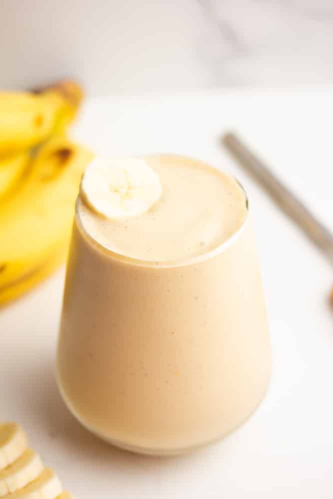 pretty glass cup full of smoothie with bananas in background