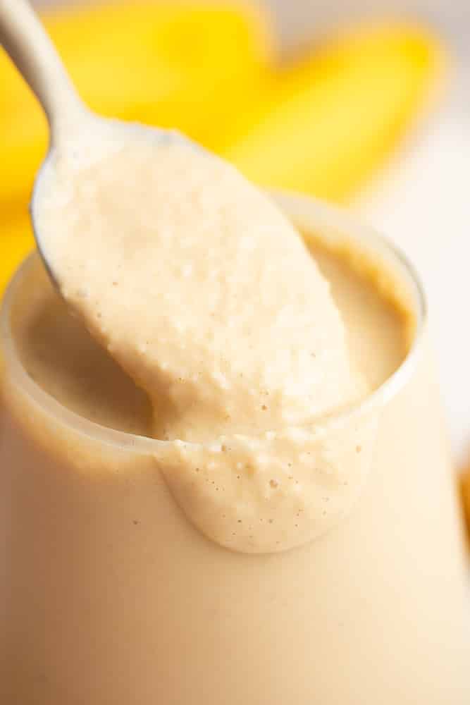 close up of a banana smoothie with a spoon in it lifting out showing the texture