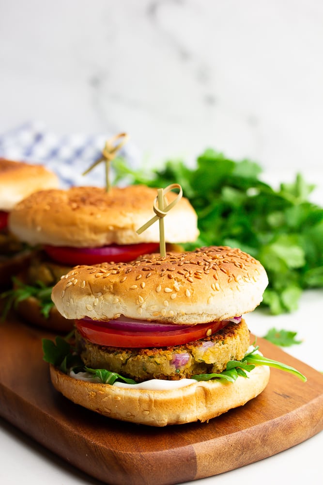 three burgers in a row on a cutting board, white marble background