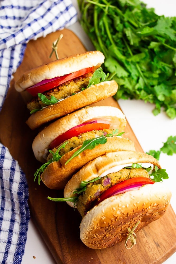 3 burgers on their sides with tomatoes, arugula on a cutting board