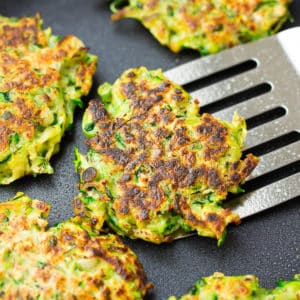 square image of a pan with fritters, one being lifted out with a spatula